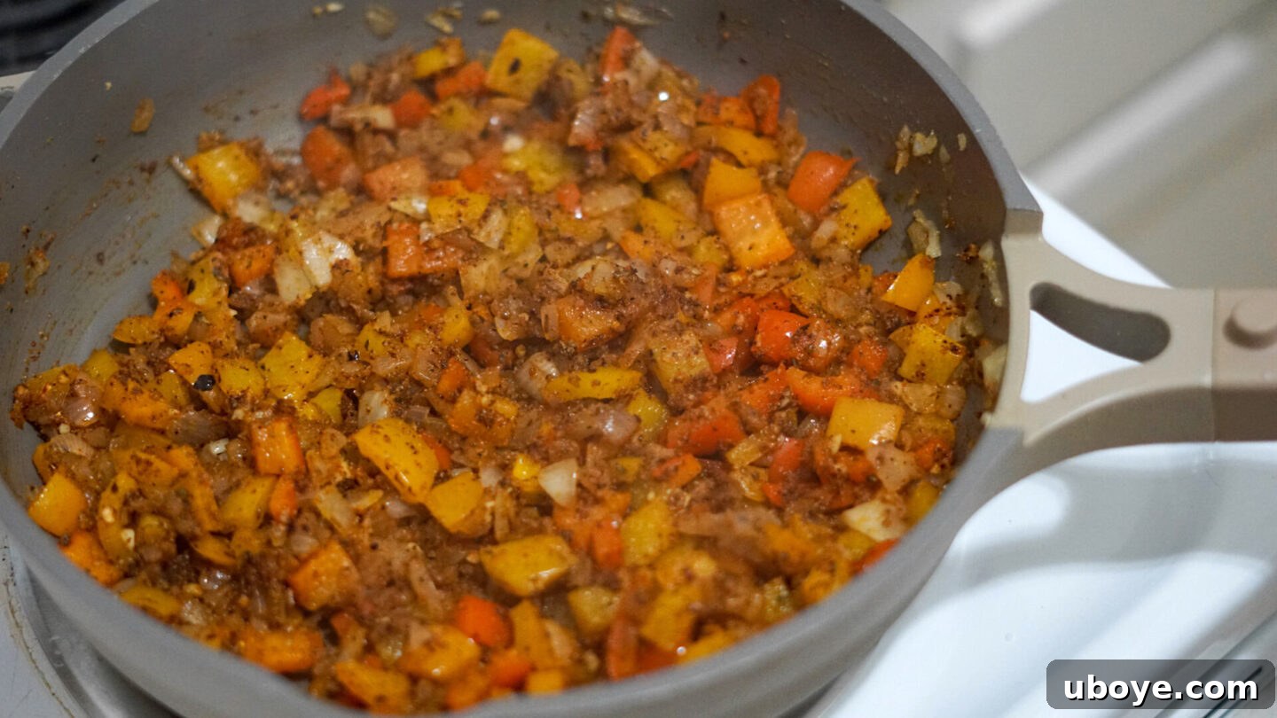 Cooked bow-tie pasta being tossed with the creamy Cajun sauce and vegetables in a large pan.