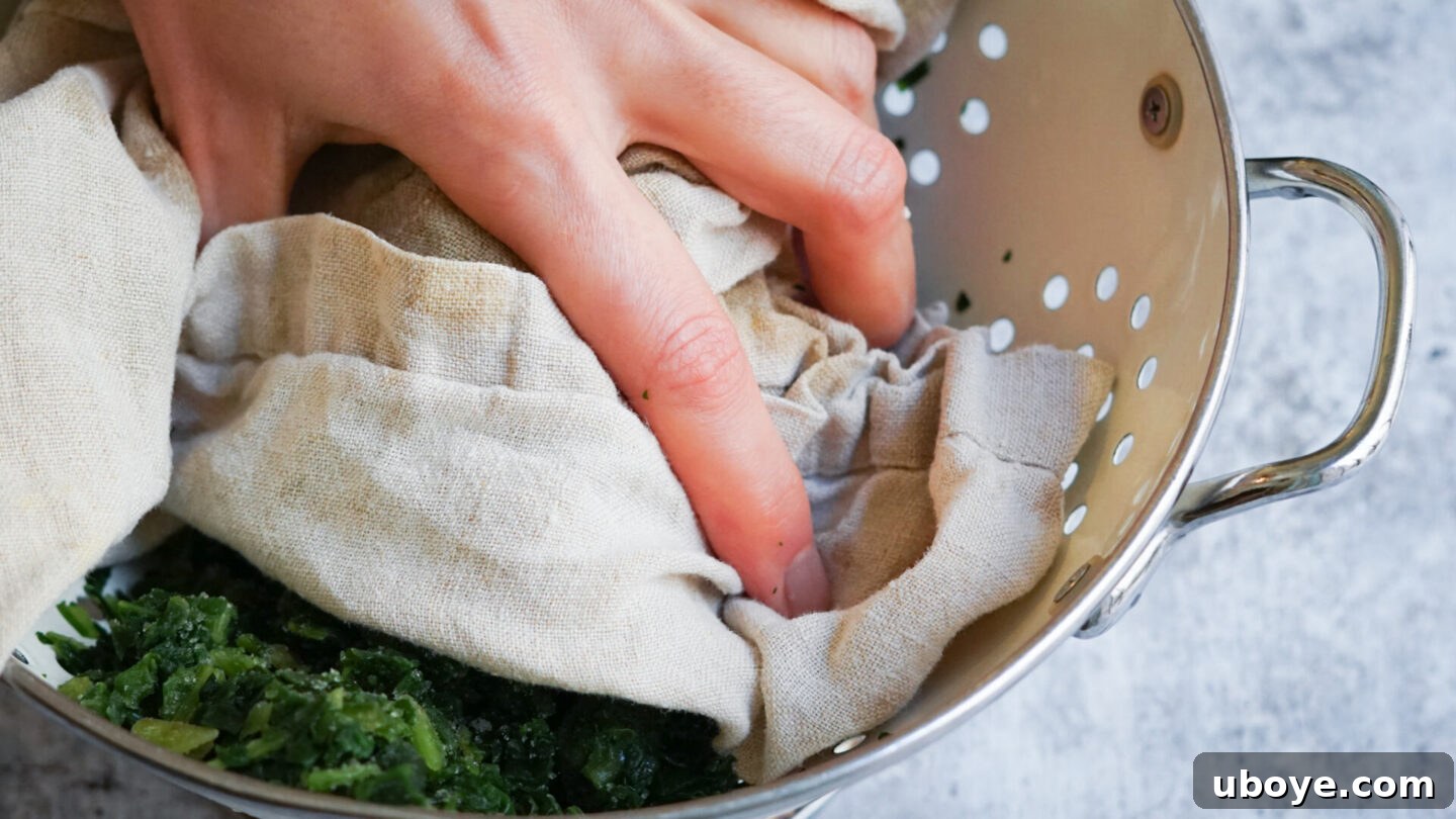 Hands squeezing excess water from thawed spinach using a clean kitchen towel.