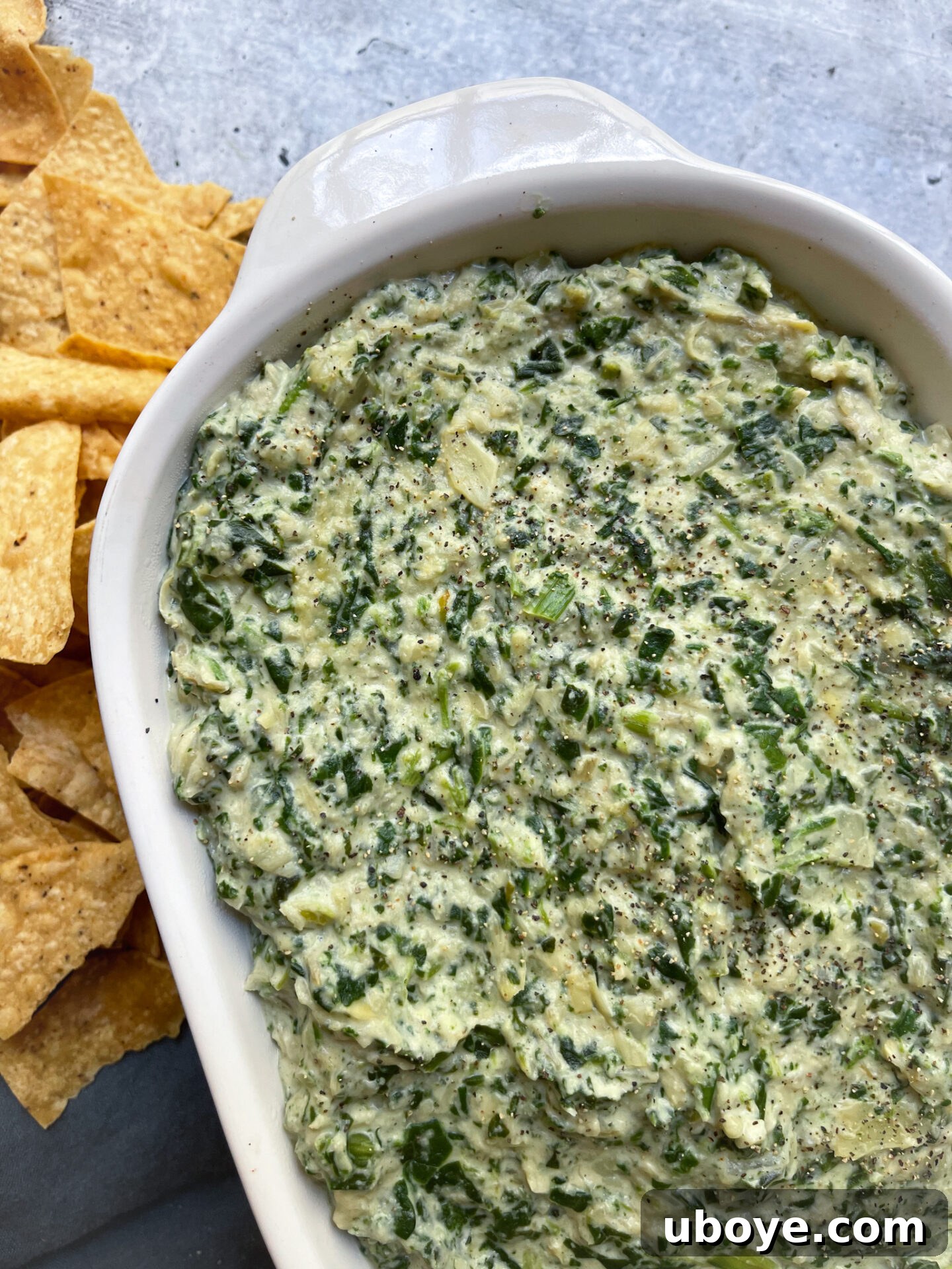 Various dippers, including crackers, tortilla chips, and fresh vegetables, surrounding a bowl of creamy vegan spinach artichoke dip.