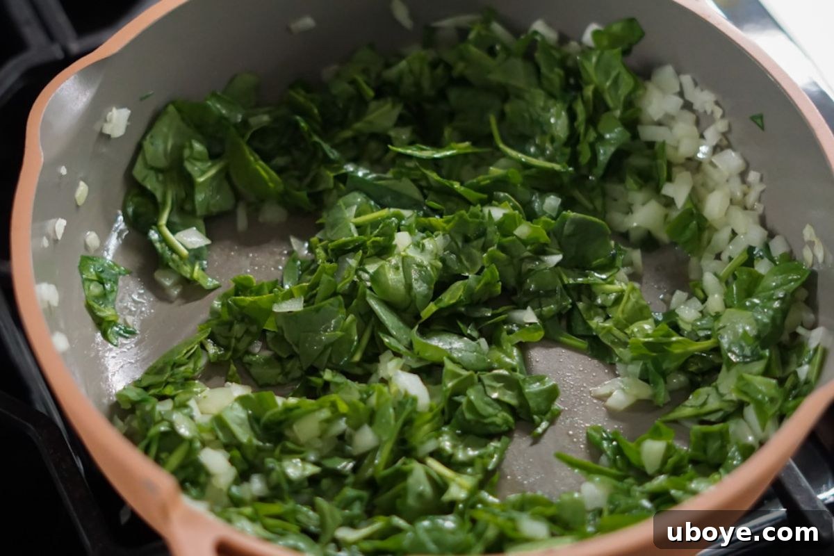 Cooked spinach and onions in a frying pan, ready for the quiche filling