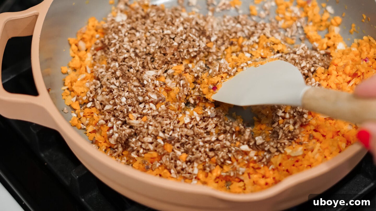 Chopped onions and carrots sautéing in a pan on the stove.