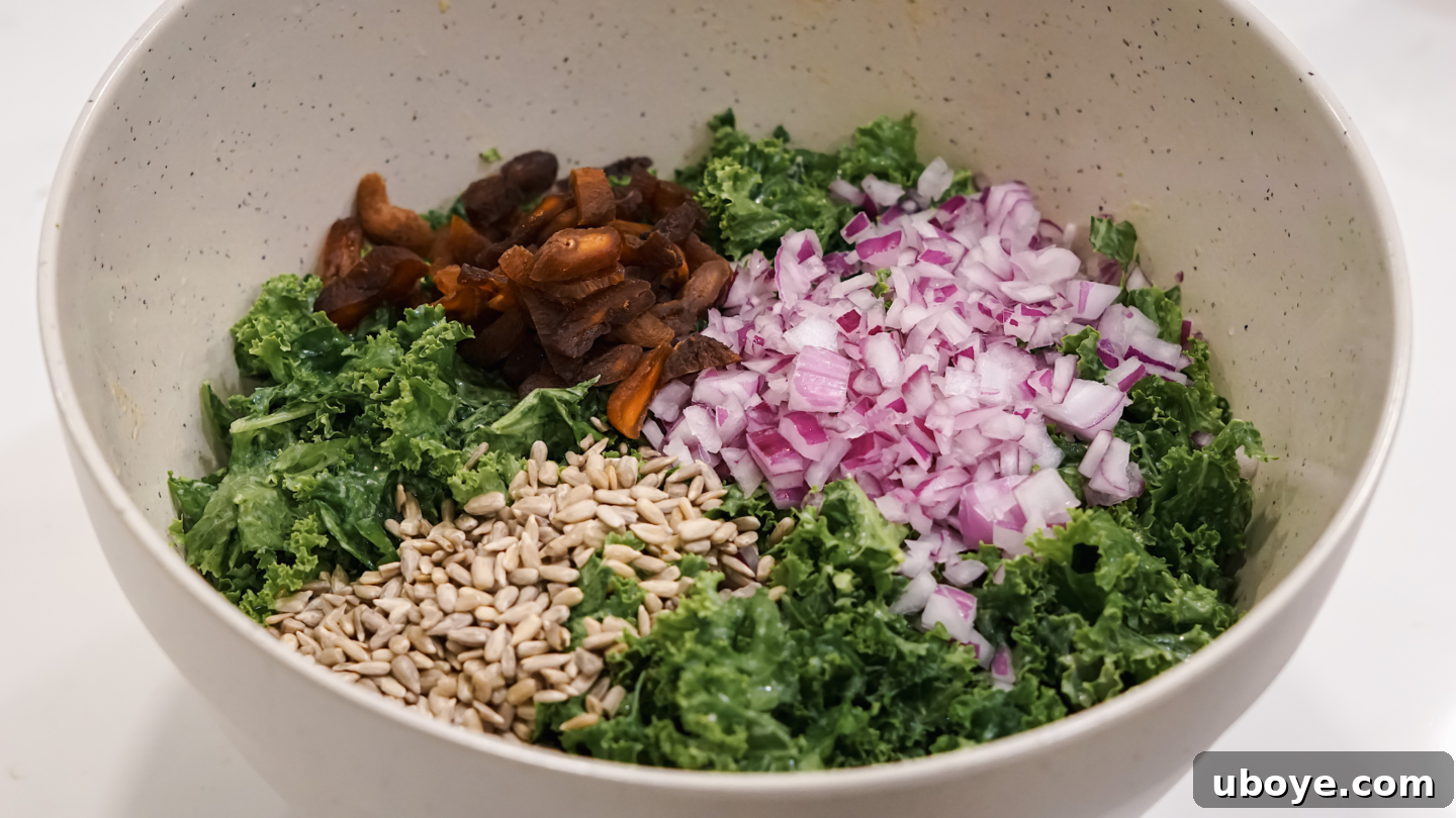 Fresh kale salad with apricots, sunflower seeds, and red onions in a mixing bowl.