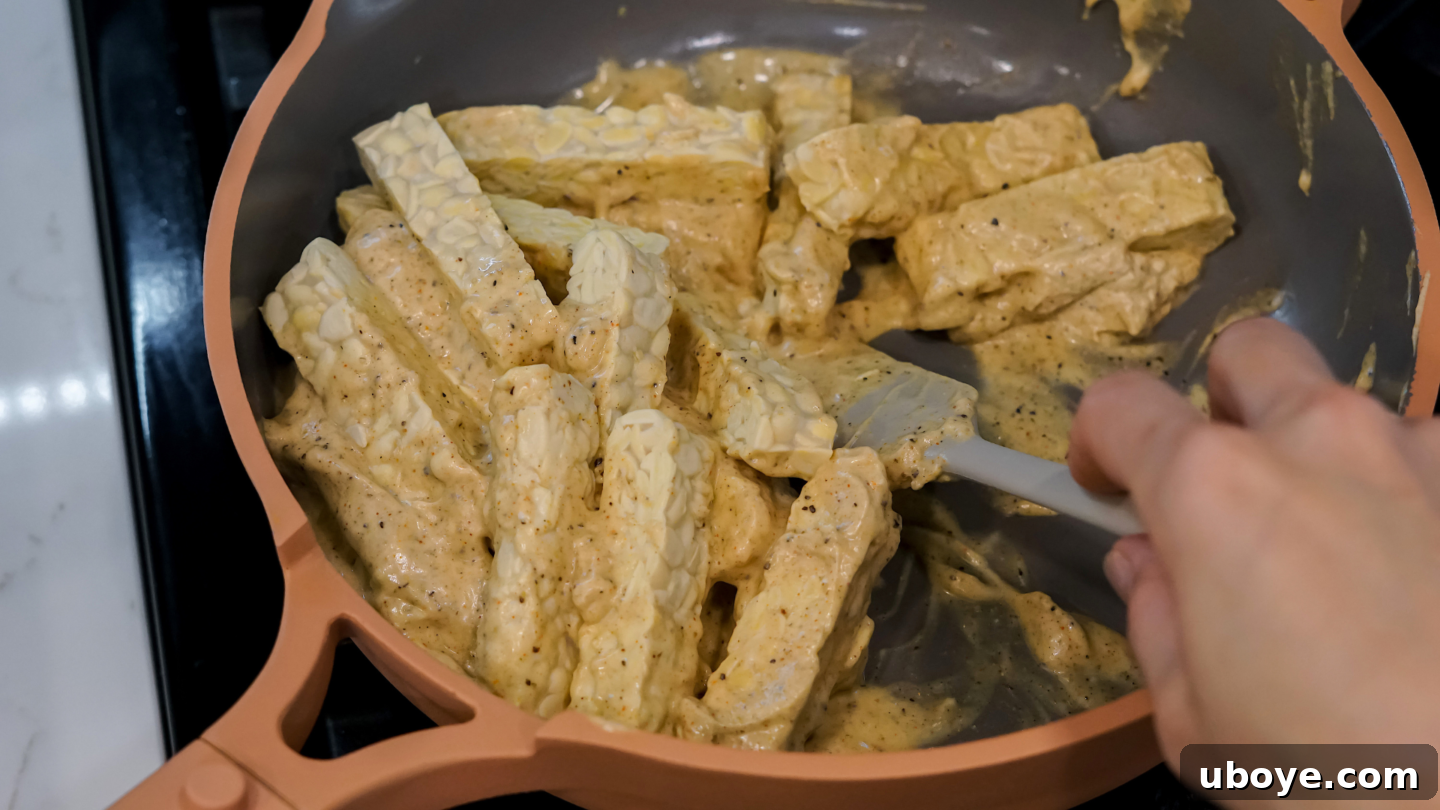Marinated tempeh strips coated in a vivid red-orange Tandoori yogurt sauce, patiently resting before the cooking process.