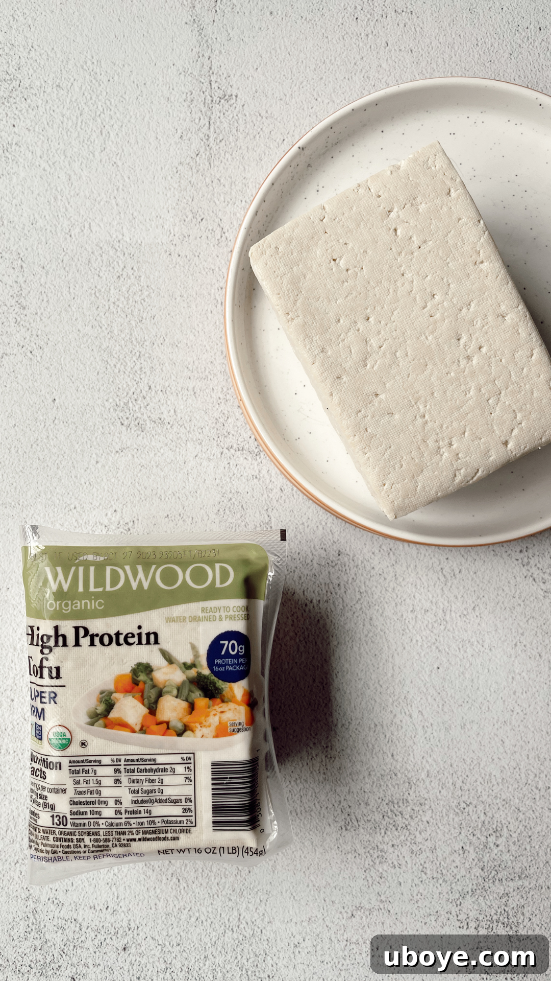 A block of firm, unpressed tofu resting on a white plate, highlighting its dense texture