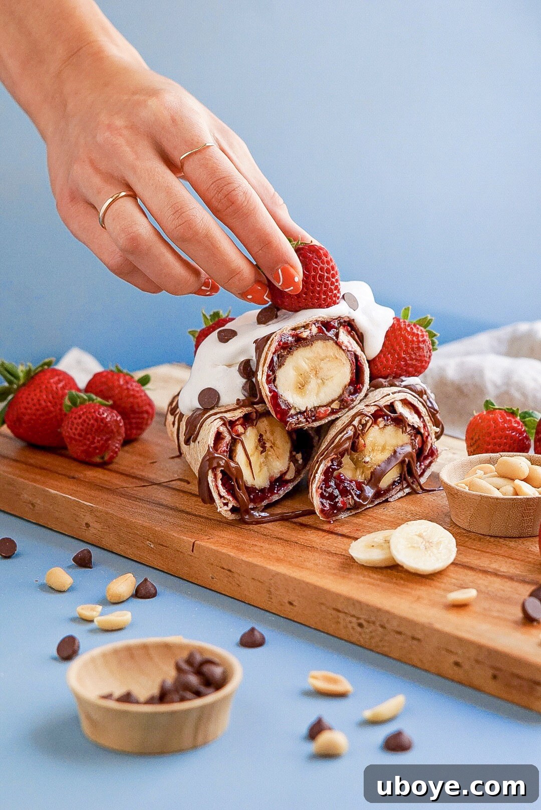 Banana Split Swirls 2 Two hands presenting a freshly made Vegan Banana Split Roll-Up, showcasing its delicious layers and toppings.