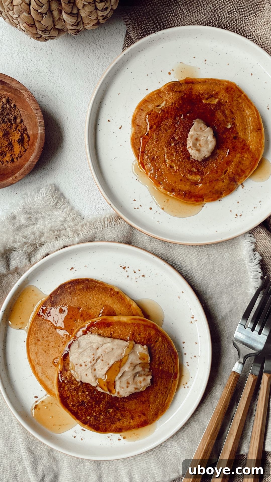 Close-up of a stack of fluffy vegan pumpkin pancakes on a white plate, ready to be topped with cinnamon butter and maple syrup.