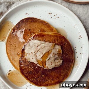 A beautifully plated stack of vegan pumpkin pancakes with a generous dollop of homemade cinnamon butter and a drizzle of maple syrup.