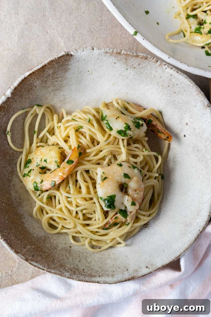 A close-up of a serving of garlic butter prawn pasta, garnished with fresh herbs