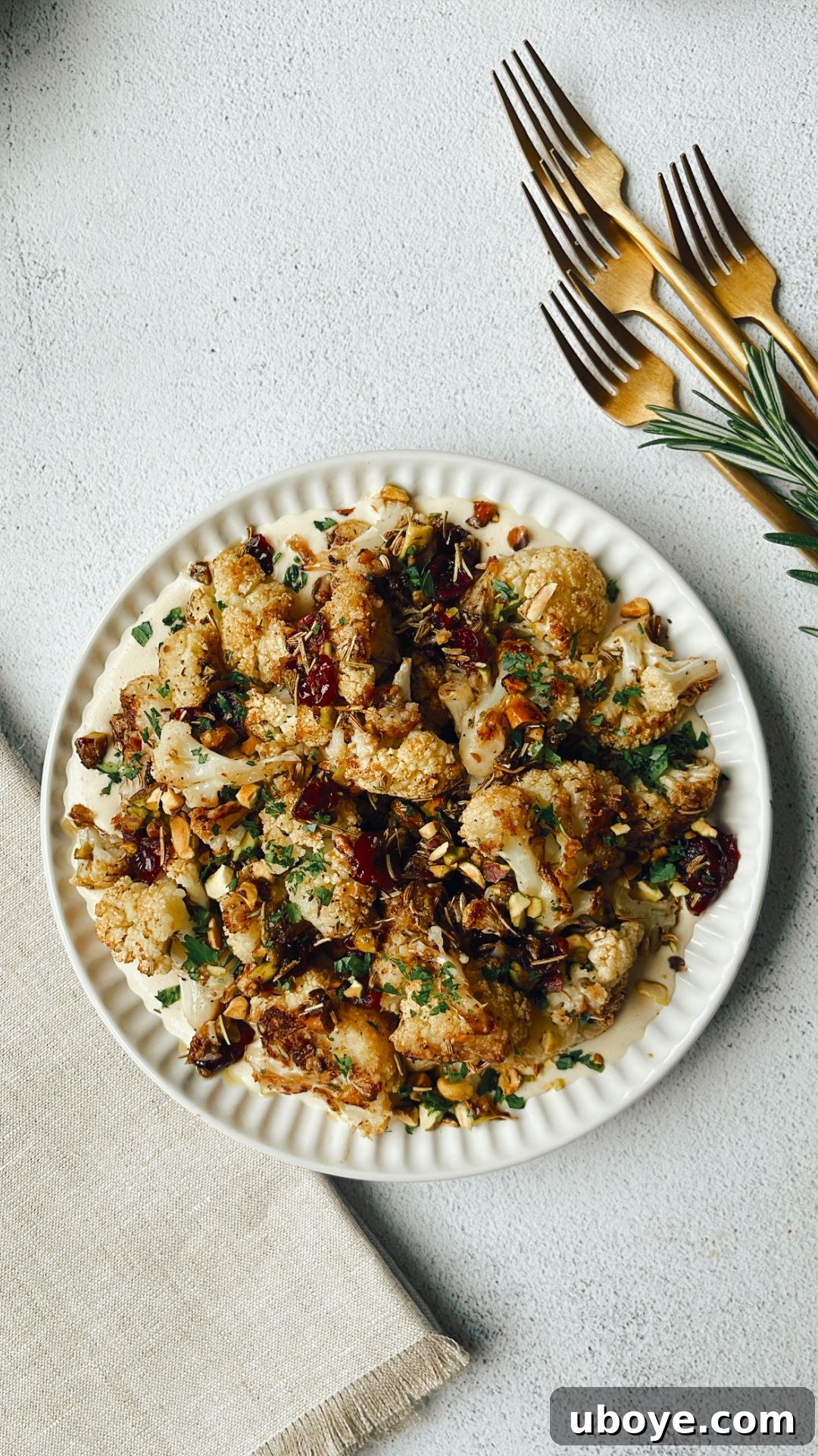 Platter of roasted cauliflower with rosemary, pistachios, and cranberries, garnished with fresh parsley and a side of dairy-free cashew cream.
