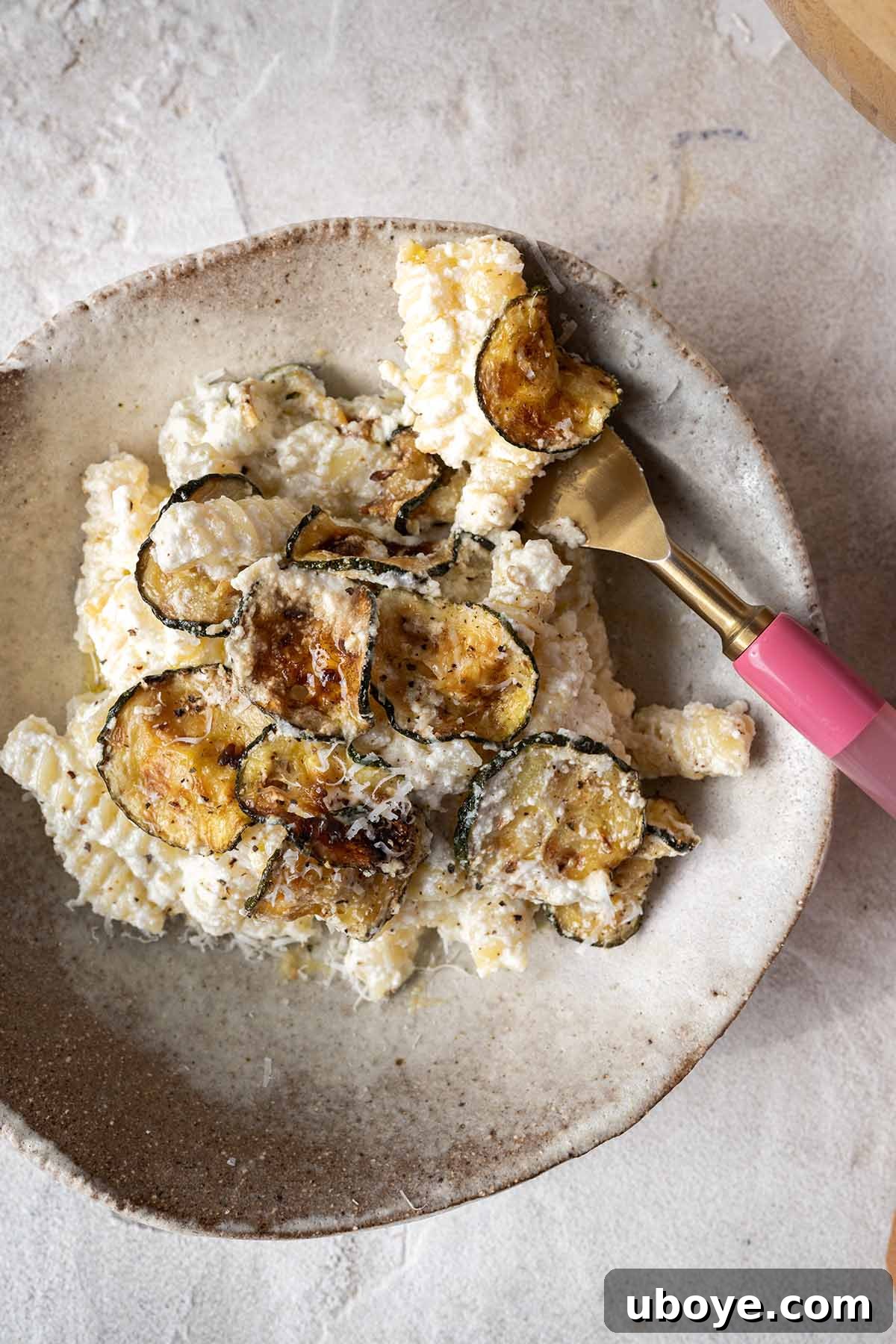 A forkful of bright, creamy lemon ricotta pasta with hints of green zucchini on a white plate, ready to be enjoyed.