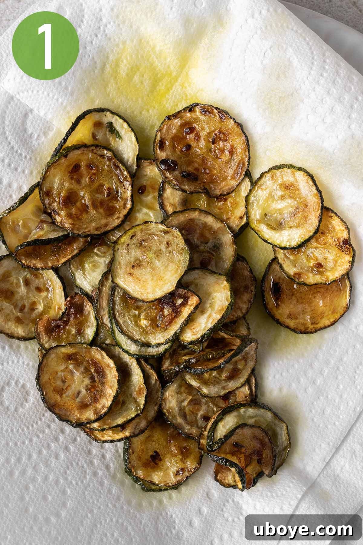 Crispy golden-brown zucchini slices draining on a paper towel-lined plate after frying, ready to be added to the pasta.
