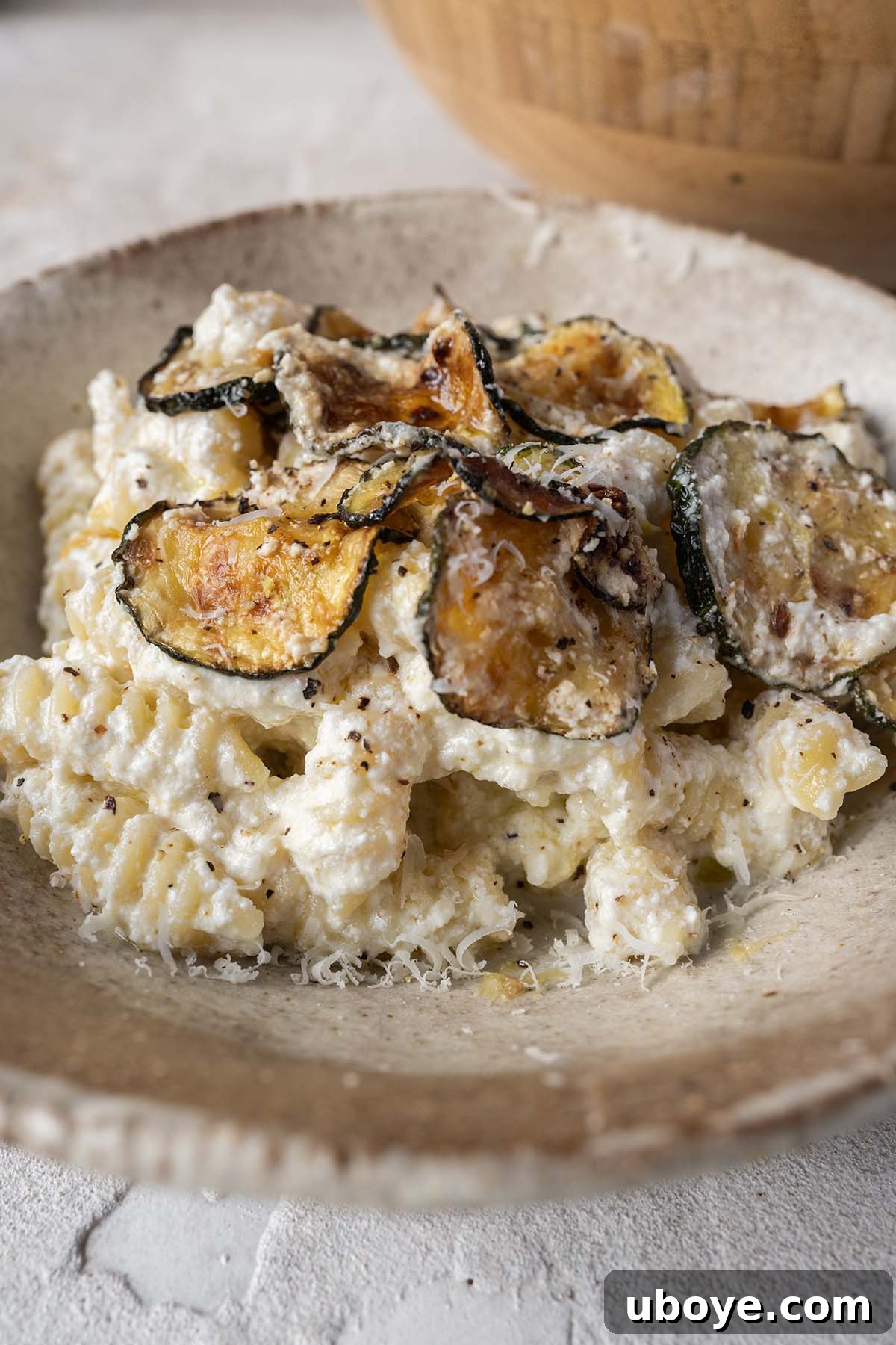A close-up shot of a plated lemon ricotta pasta, beautifully garnished with crispy zucchini slices, fresh herbs, and a light dusting of cheese.