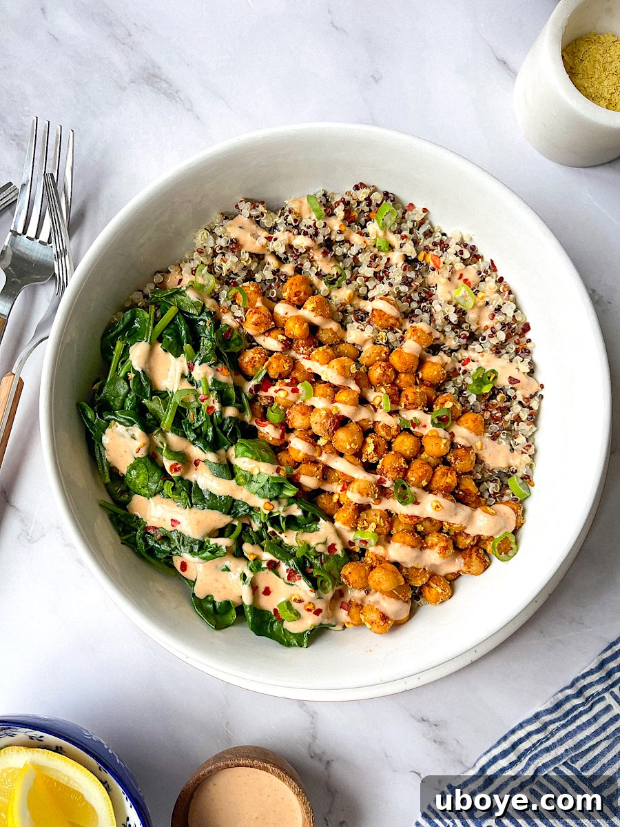 A vibrant Quinoa Protein Bowl topped with roasted chickpeas, spicy spinach, and drizzled with creamy tahini chili sauce.