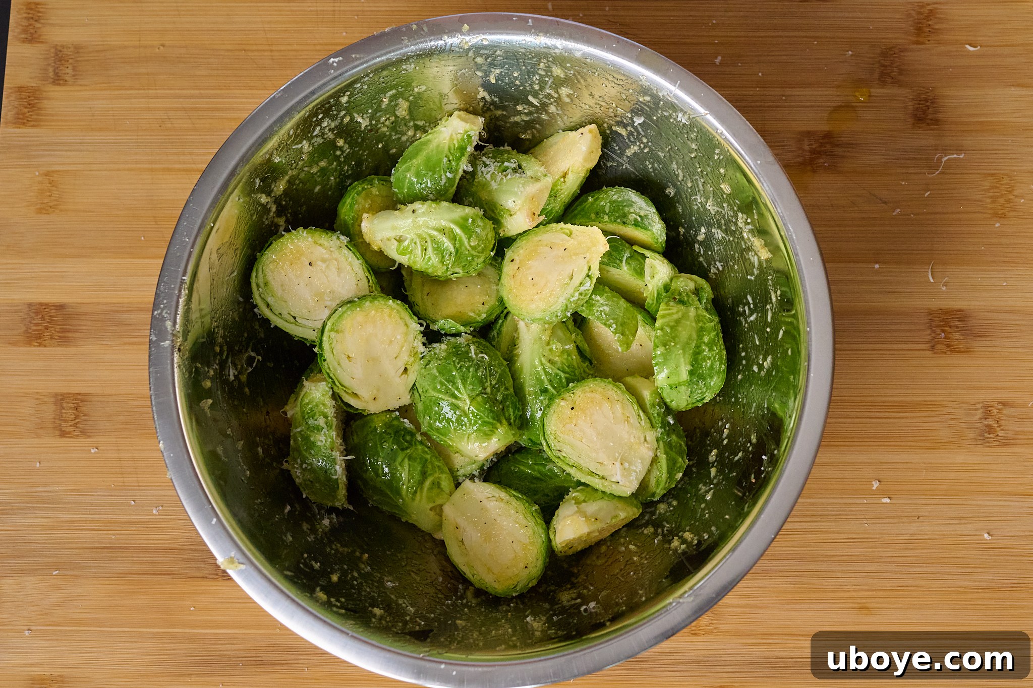 Brussels sprouts have been sprinkled with parmesan and olive oil and sit in stainless steel bowl.