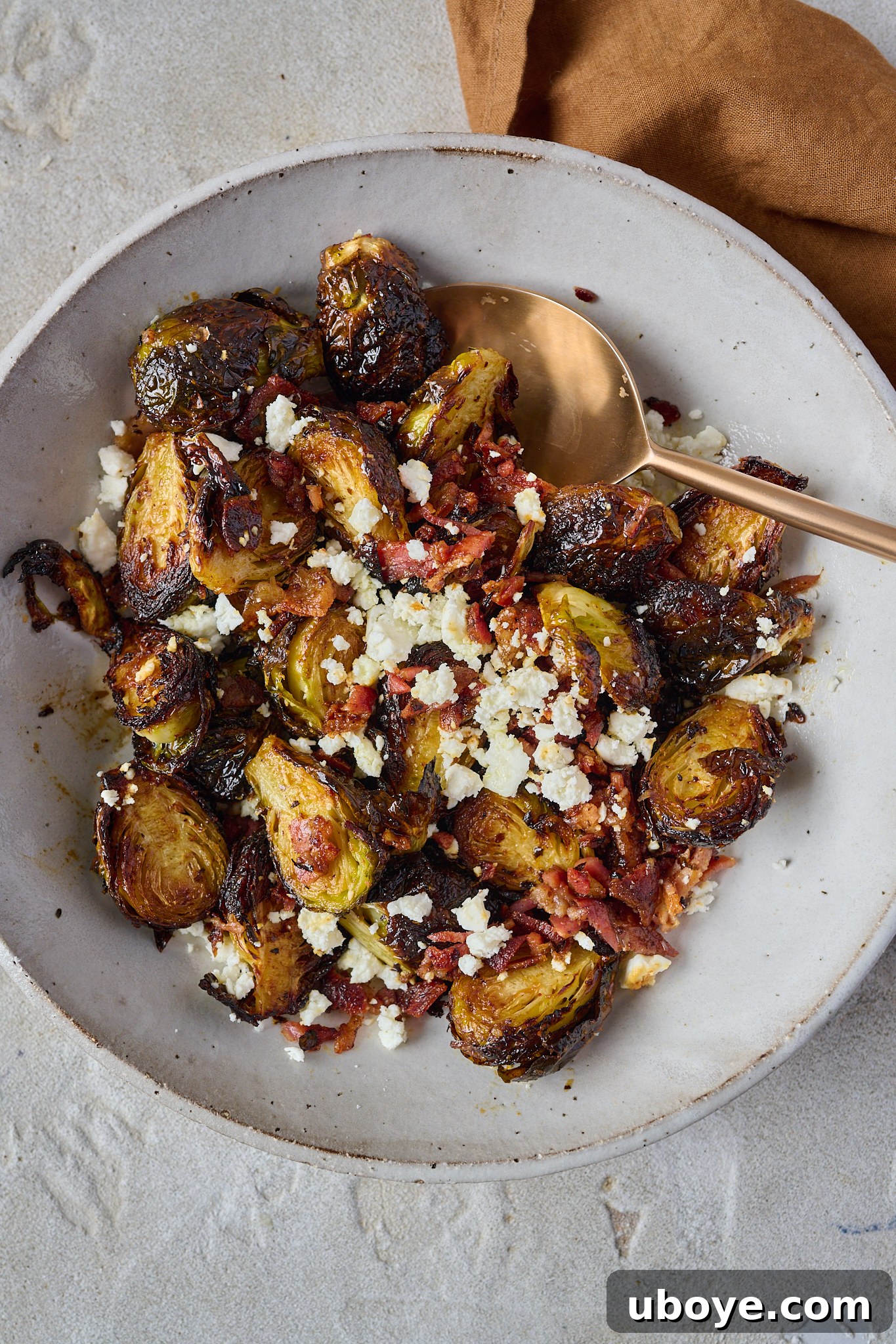Crispy Brussels sprouts with bacon and feta crumbled on top in a large white bowl.