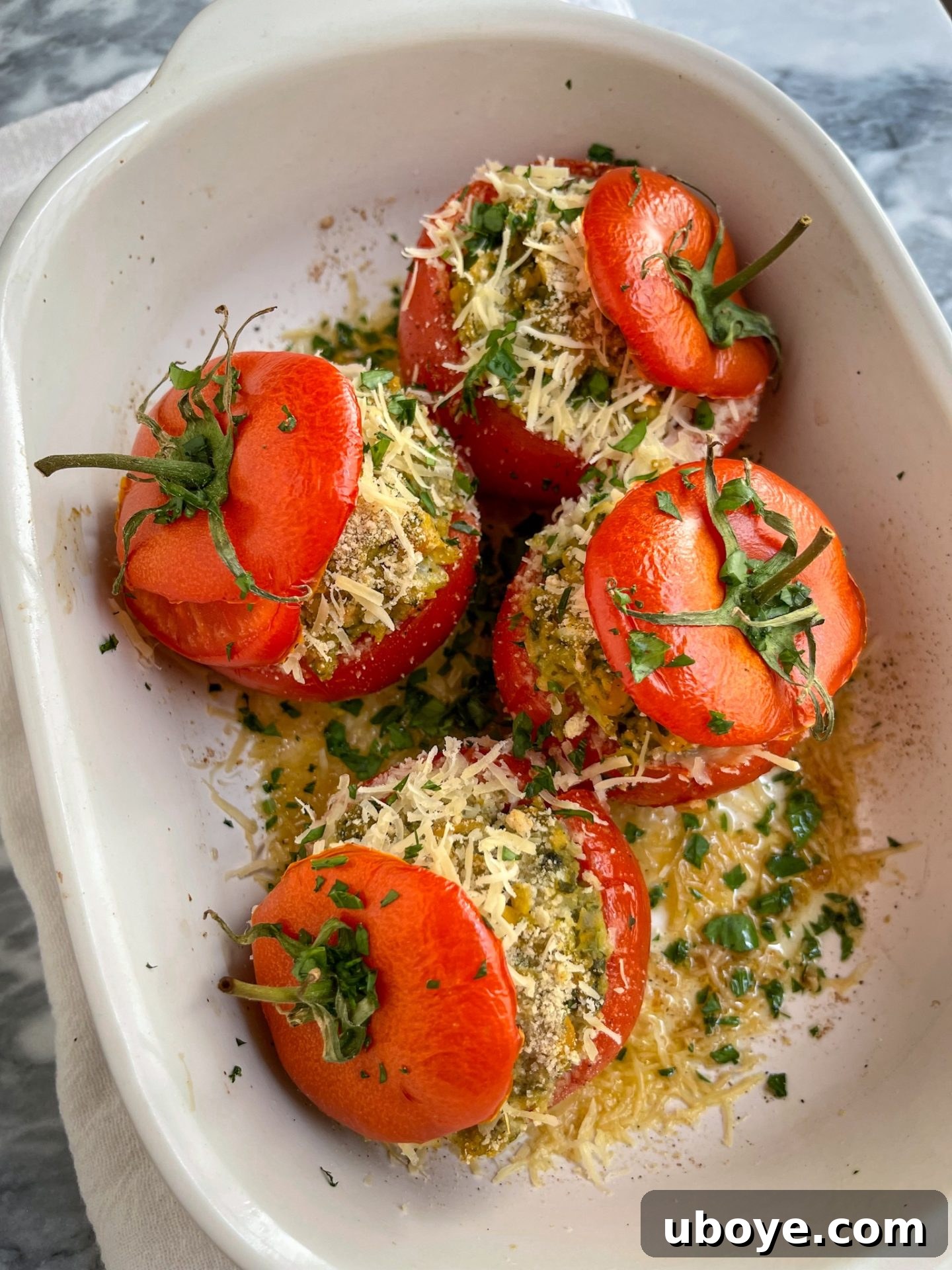 5 Effortless Summer Dinners 2 Beautifully baked pesto stuffed tomatoes presented in a pristine white casserole dish, artfully garnished with fresh basil leaves, ready to be enjoyed.