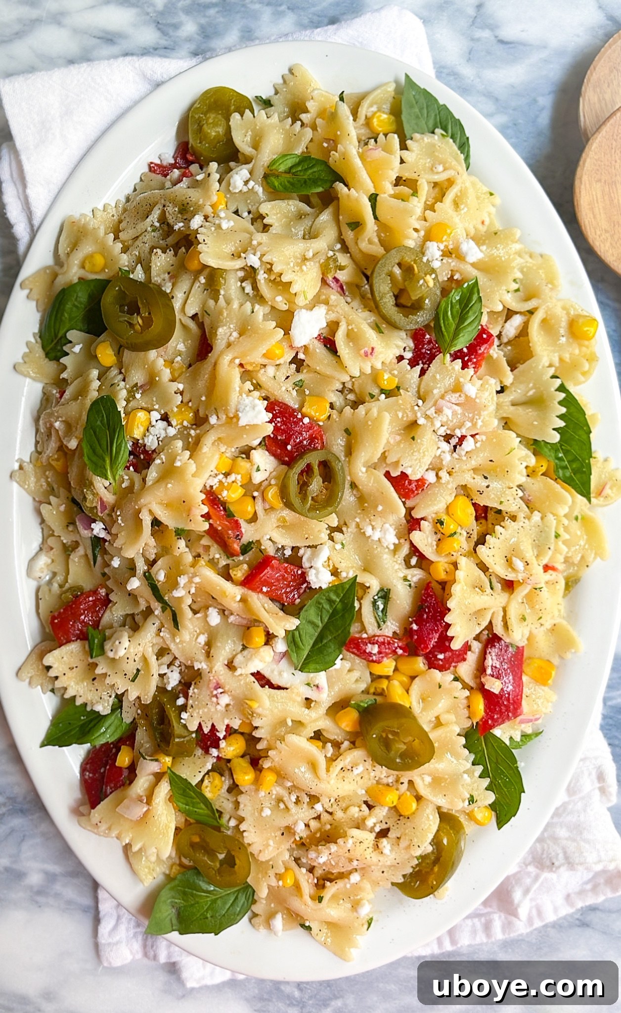 5 Effortless Summer Dinners 3 A vibrant and refreshing jalapeño and sweet corn pasta salad, richly garnished with fresh basil and red peppers, elegantly presented on a white plate and ready for al fresco dining.