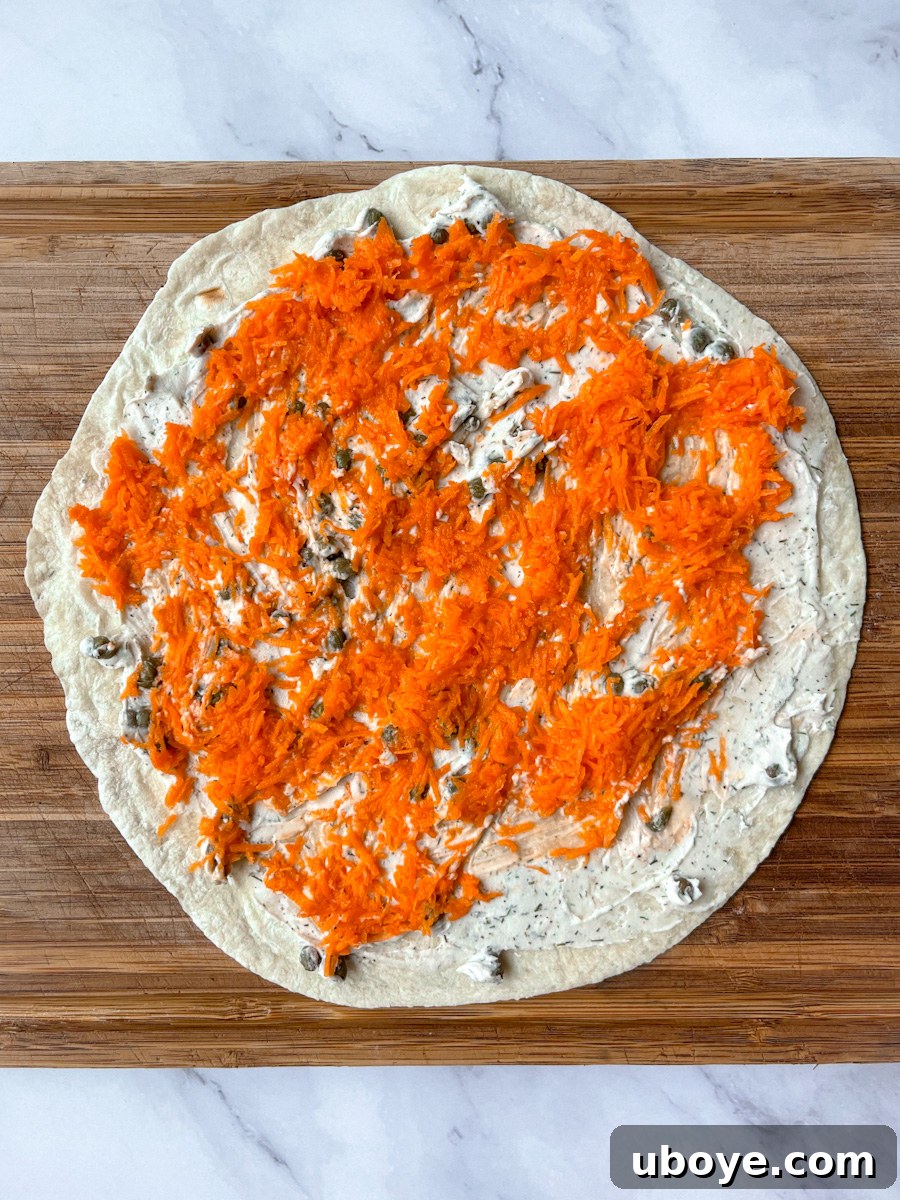 Effortless Pinwheel Creations 5 Assembling a tortilla pinwheel with vegan cream cheese, marinated carrots, spinach, and red onion layers