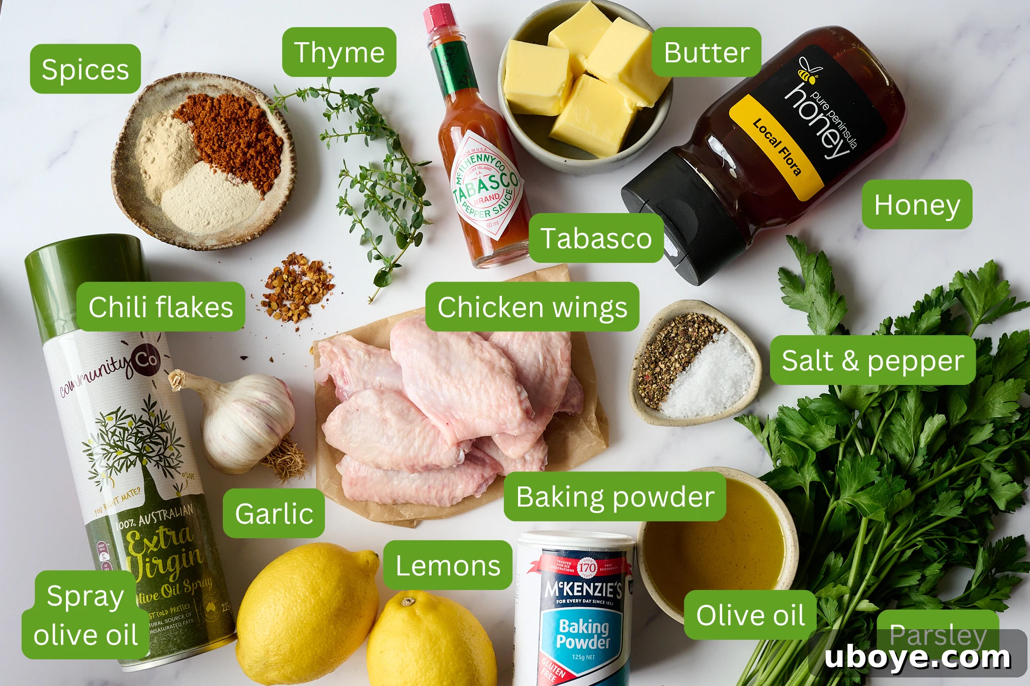 List of ingredients layed out on a board. Picture includes the items: spices, thyme, tabasco, butter, honey, chicken wings, chili flakes, salt and pepper, olive oil, parsley, baking powder, lemons and garlic.