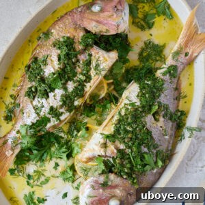 A succulent whole baked snapper with salsa verde, garnished with fresh herbs and lemon, presented as a finished dish.