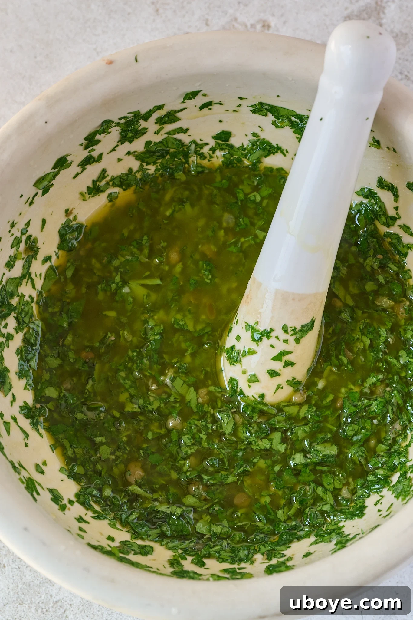 A pristine white mortar and pestle containing freshly made, vibrant green salsa verde, highlighting its fresh ingredients and ready to be served alongside the fish.