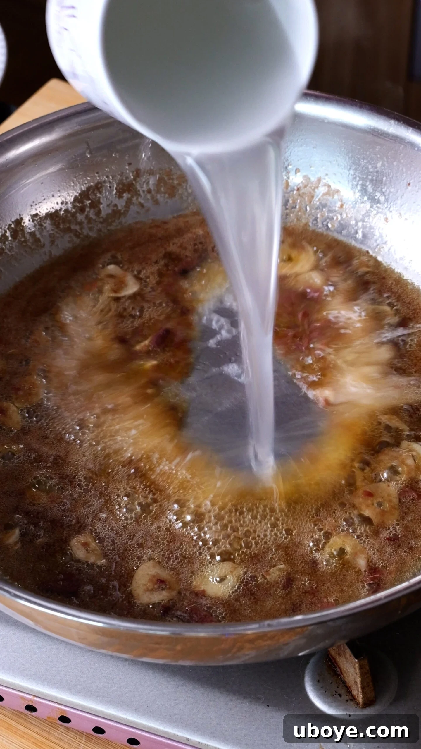 Decadent 10-Minute Anchovy Butter Pasta 7 Pasta water is being carefully added to the anchovy butter sauce in a large stainless steel pan, creating a glossy emulsion.