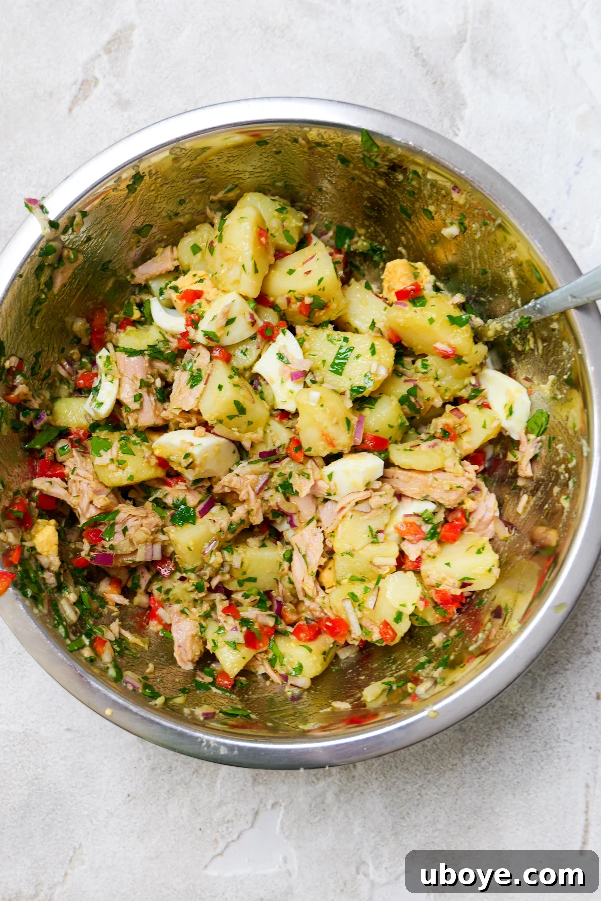 Stainless steel bowl shows everything for spanish potato salad all mixed together. 