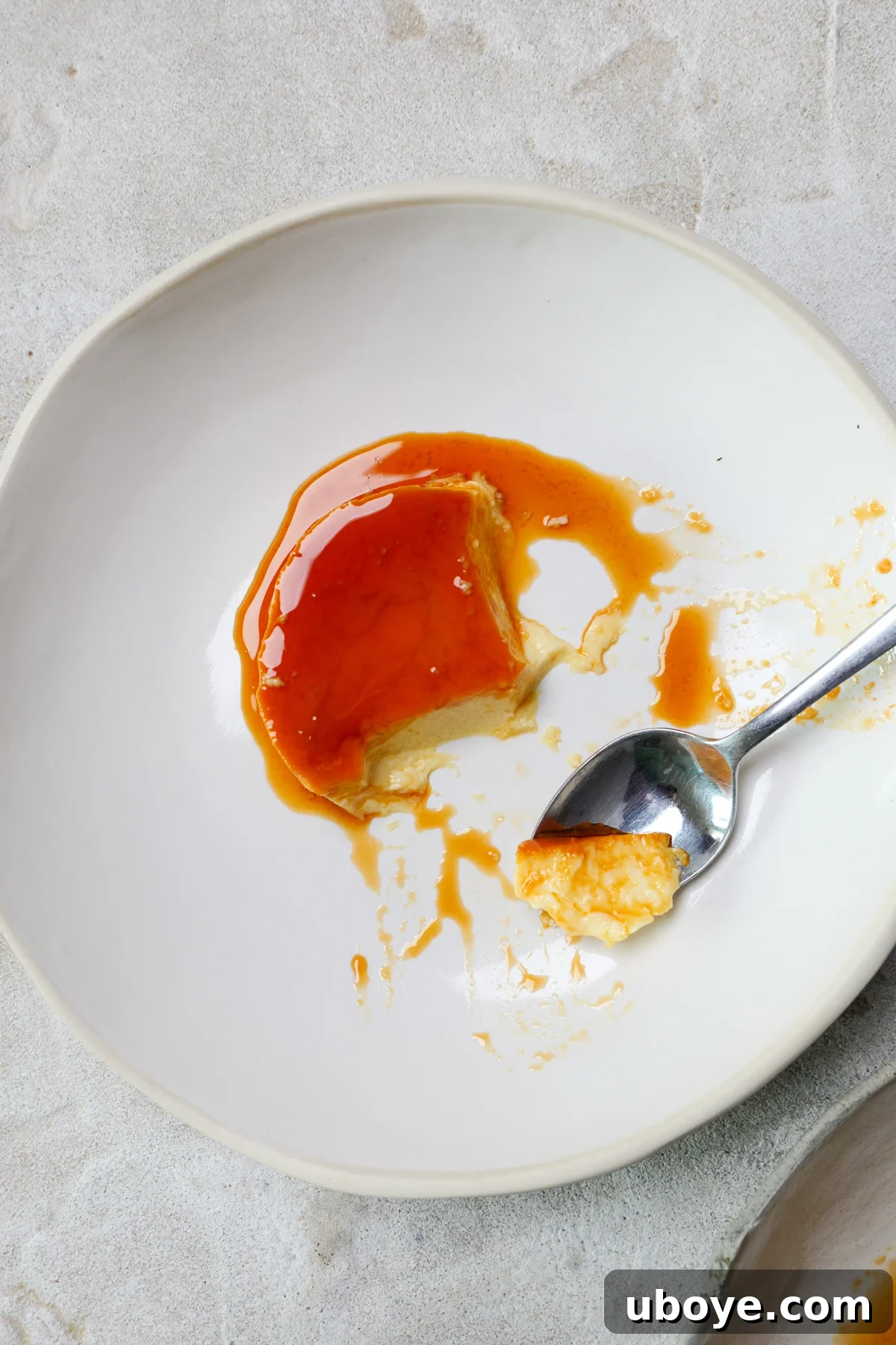 Classic Spanish Flan Recipe: Smooth Caramel Custard You’ll Love 8 Spanish flan is in large white bowl with golden custard drizzled all over. A silver spoon has broken into the flan.